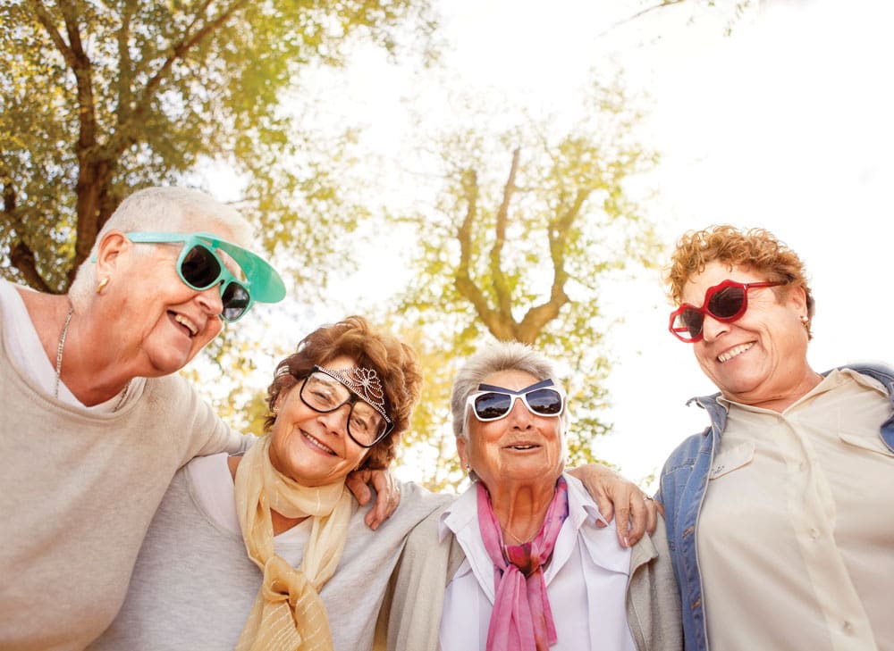 Group of older women wearing fun sunglasses pose with their arms around each other Group of older women wearing fun sunglasses pose with their arms around each other