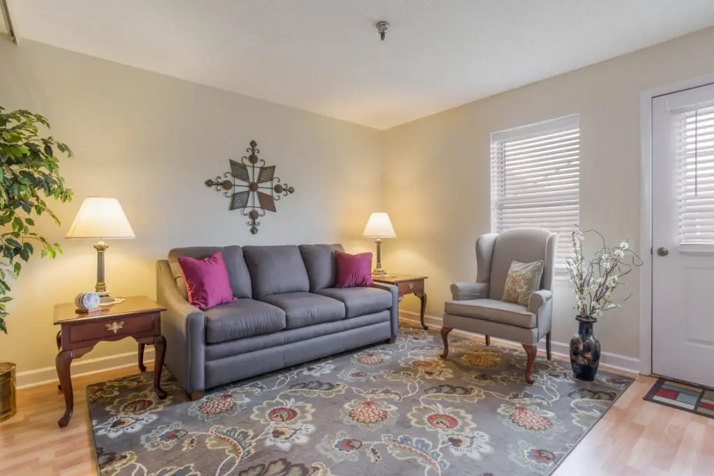 Living area with sofa, chair, rug, window, lamp, various decorations, and door to the outside