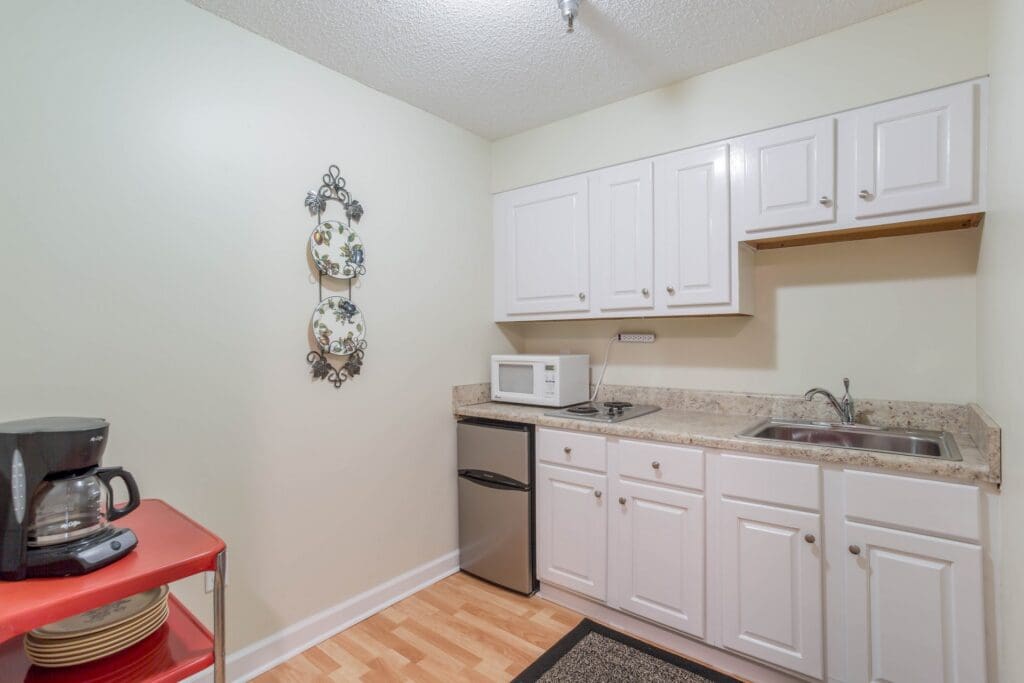 Neutral-toned kitchen area with white cabinets, a fridge, coffee maker, microwave, sink, and hot plate