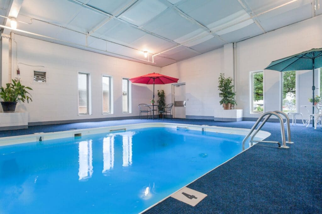 Side view of indoor swimming pool, tables and chairs area, and multiple floor-to-ceiling windows